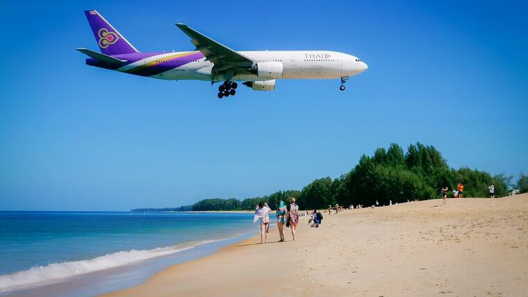 Самолёт Thai Airways низко над пляжем Май Кхао у аэропорта Пхукета, по песку гуляют туристы