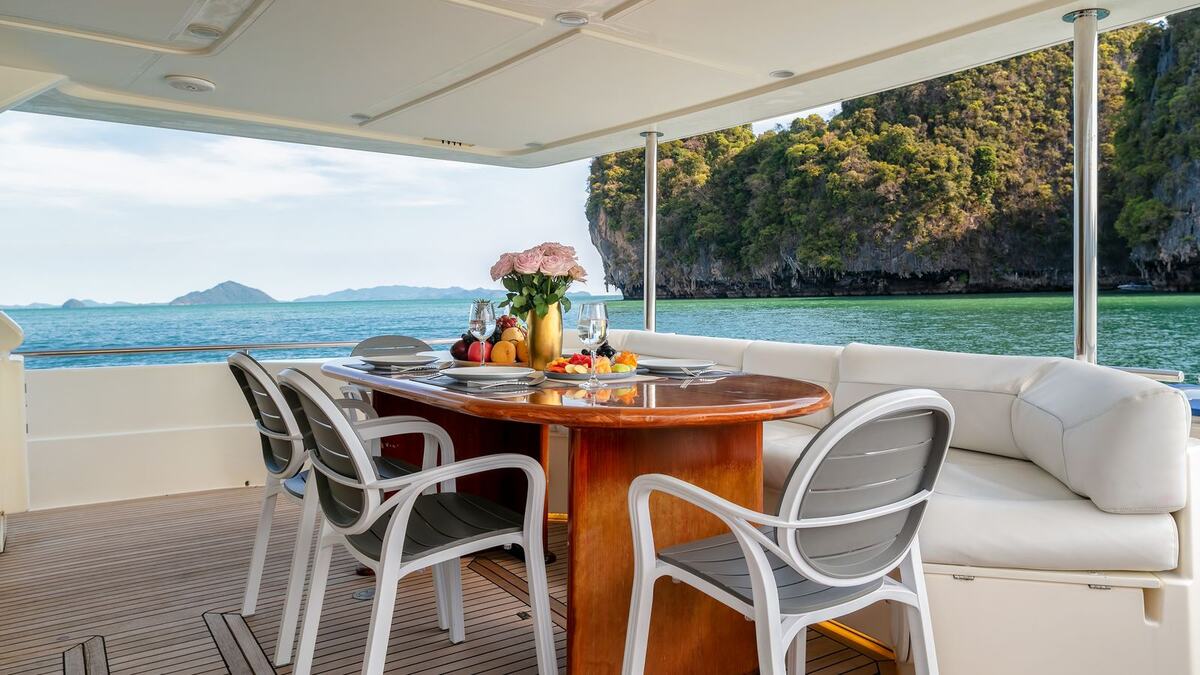 Обеденный стол на корме яхты Ferretti 80 Sofia, за бортом скалистый остров